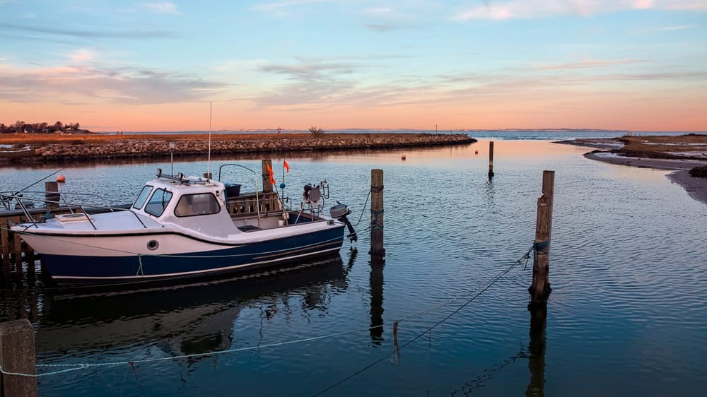 Tranquil harbor sunset—calm waters, a docked boat, and the sky painted in pastel hues.