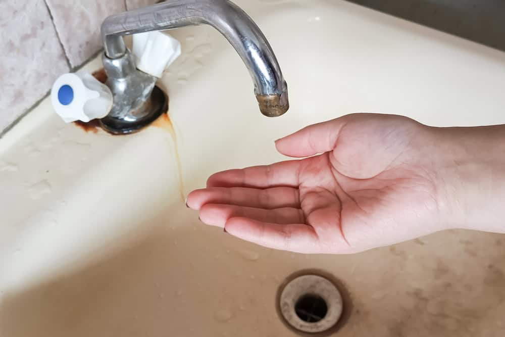 Rusty water flows from the faucet into a cupped hand, highlighting the need for plumbing maintenance.