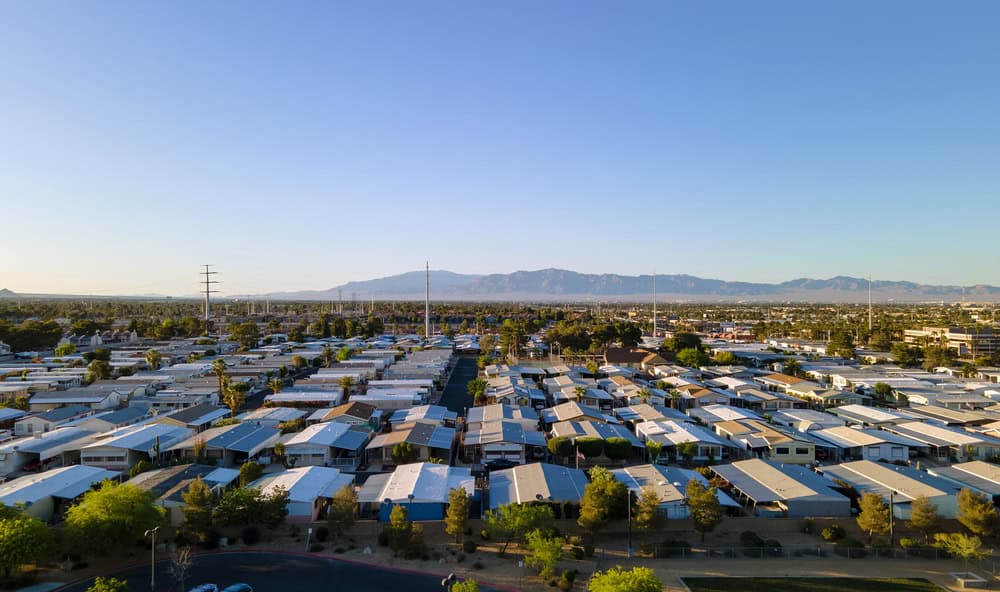 A sprawling mobile home community basks in the golden light of a clear day, with mountains in the distant horizon.