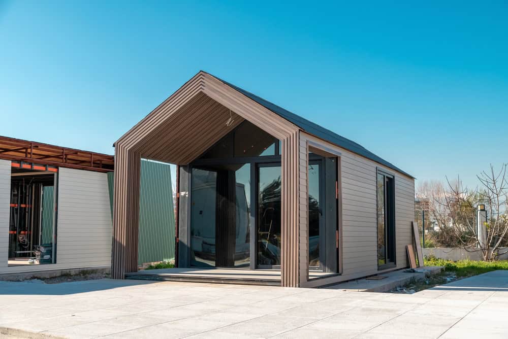 Modern minimalist cabin with sleek wooden accents and large glass doors, set against a bright blue sky.