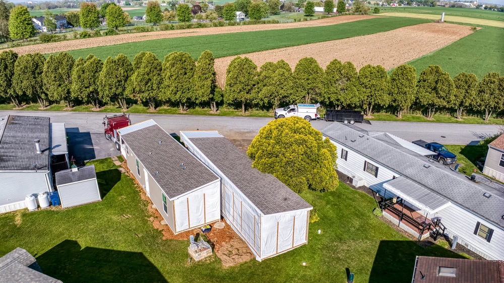 A serene countryside mobile home community surrounded by lush greenery and expansive fields.