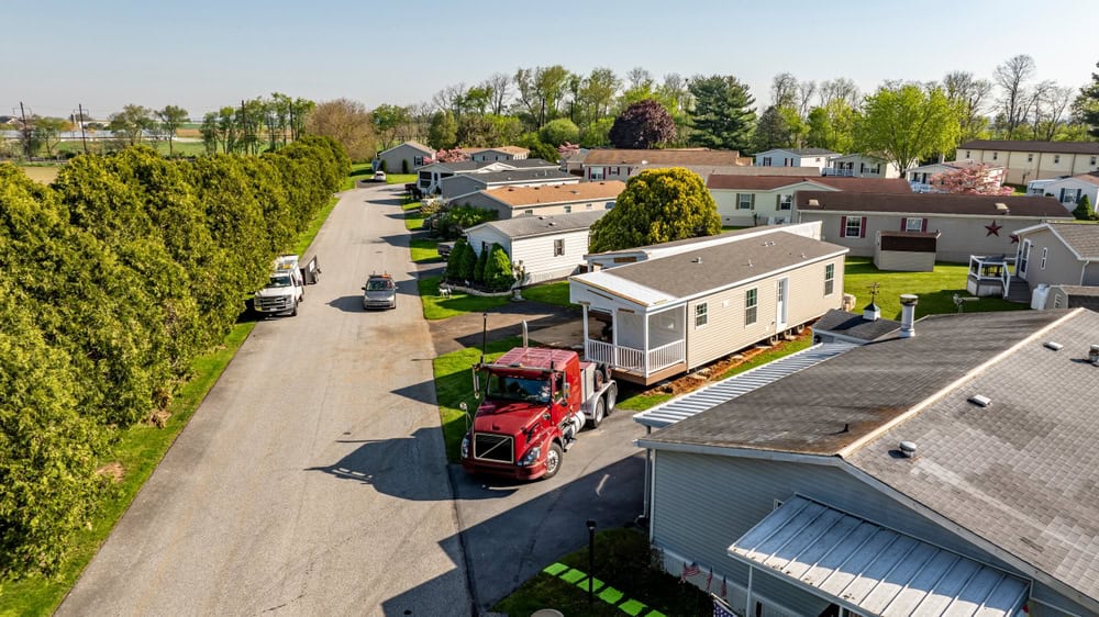 A red truck delivers a new home to a peaceful mobile home community.