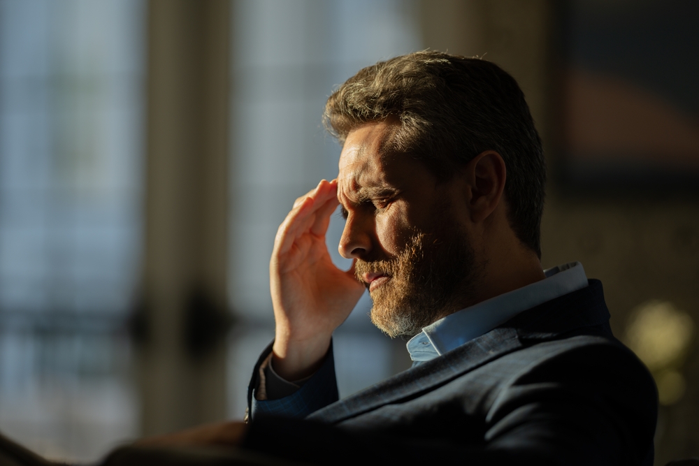 A man in a suit sits in with a headache