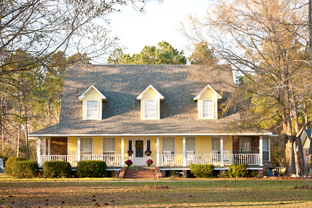 Charming yellow house with a cozy front porch nestled among tall trees.