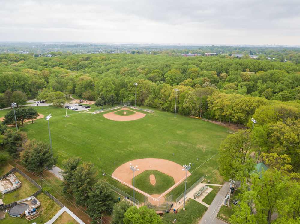 A serene aerial view of a baseball field nestled within a lush, green park, capturing the essence of community recreation and nature's beauty.