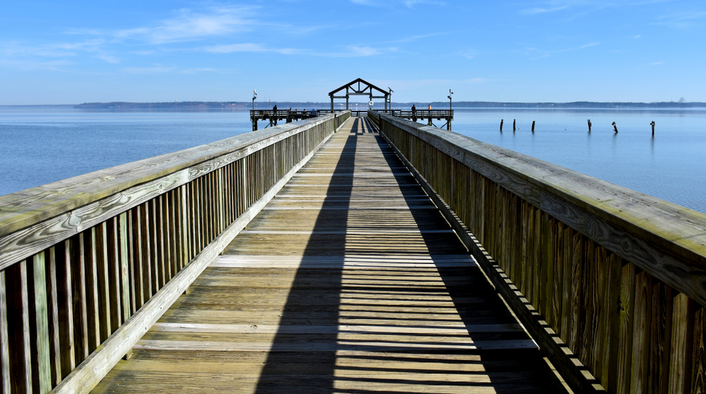 A serene wooden pier stretching into the tranquil waters under a bright blue sky.