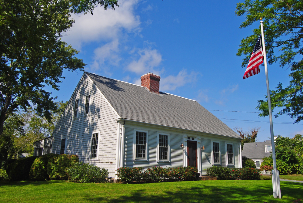 Charming Colonial home adorned with lush greenery under a vibrant blue sky, proudly displaying the American flag.