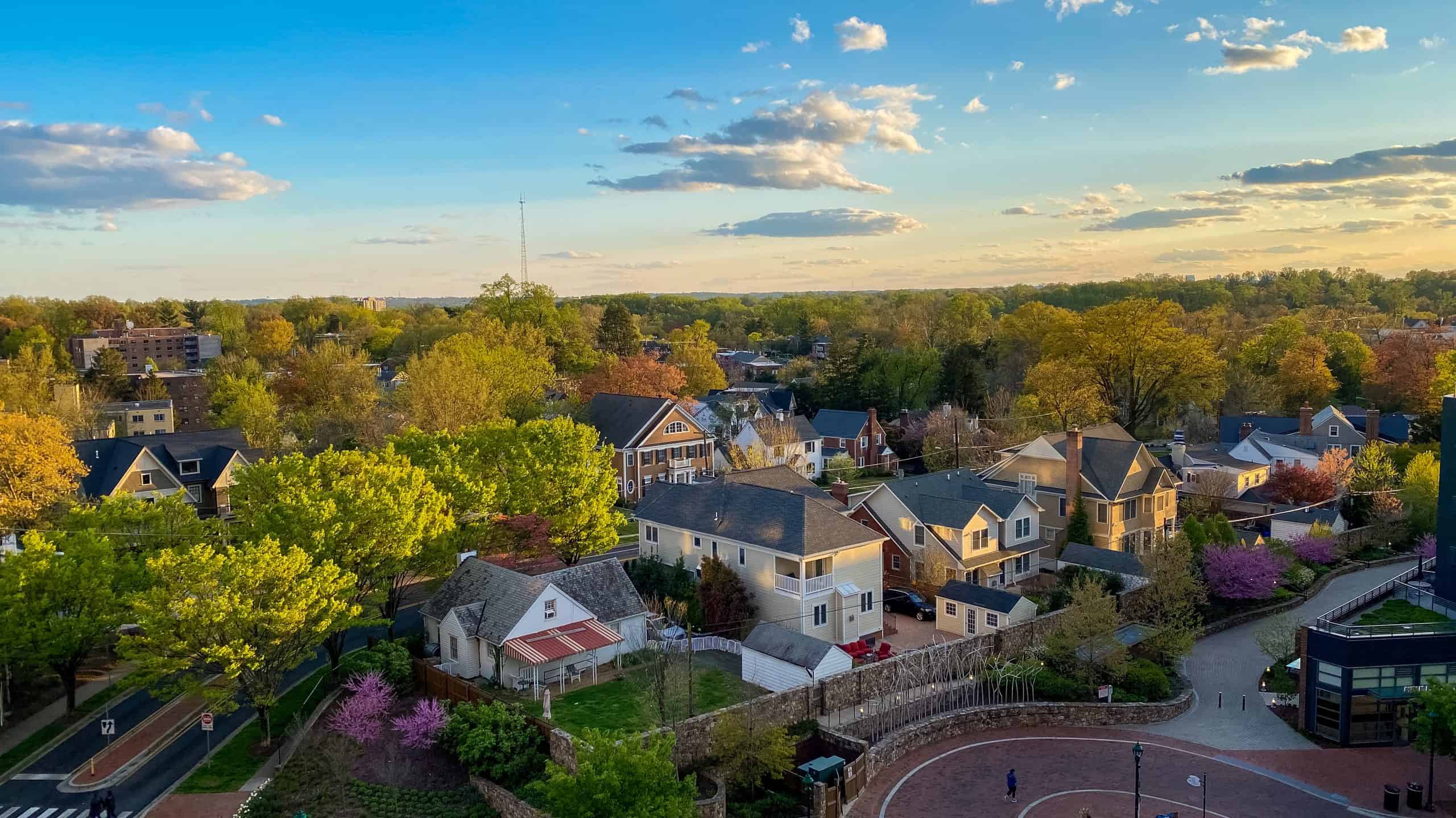 Spring sunset illuminates a charming suburban neighborhood, where blooming cherry trees and fresh foliage frame historic homes along curved streets, creating a picturesque slice of American small-town life.