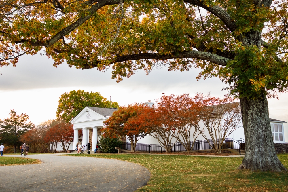 Fall colors frame a white building with pillars and a path leading to the entrance.