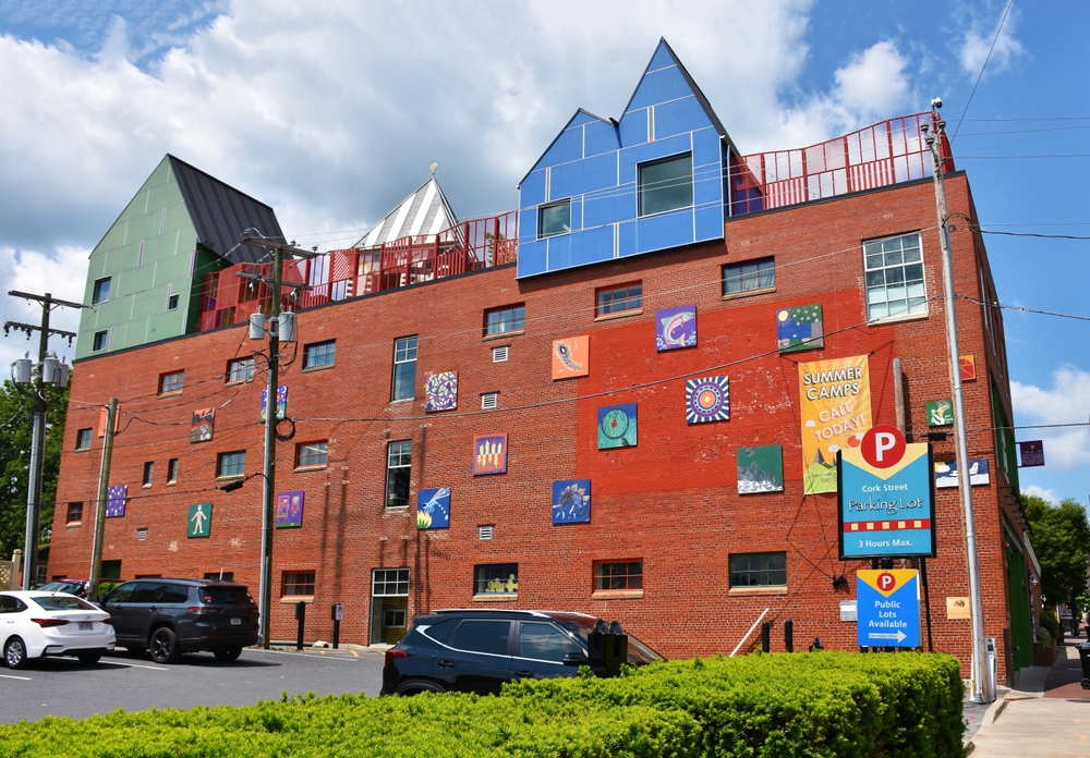 Colorful murals adorn this brick building in Cork Street, advertising summer camps. A parking lot sign warns drivers of a 3-hour maximum.