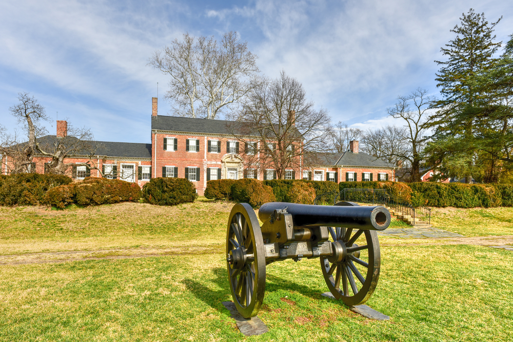 A cannon sits in front of a historic brick mansion.