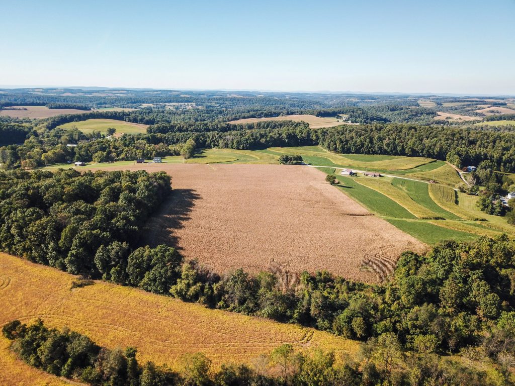 A breathtaking aerial view of lush farmlands amid rolling hills and dense forests, under a clear blue sky.