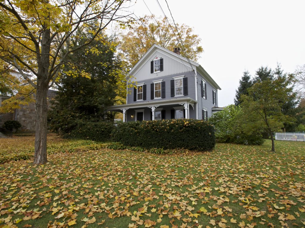 Golden leaves blanket the yard of a charming, gray Victorian house in the heart of autumn.