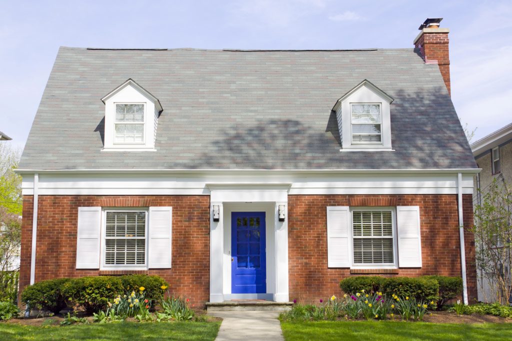 Charming brick home with a vibrant blue door, framed by spring flowers and pristine landscaping.