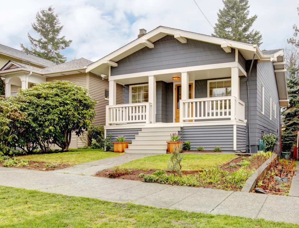 Charming gray bungalow with a cozy front porch and a well-manicured lawn.