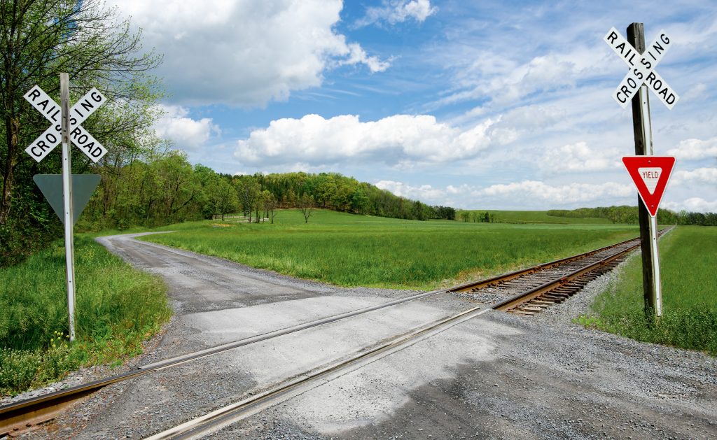 A serene rural railroad crossing amidst lush green fields and a bright blue sky.