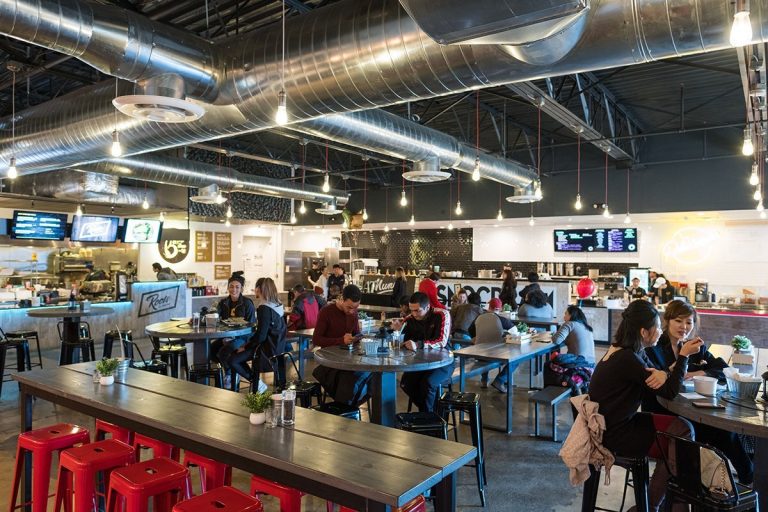 A vibrant food hall bustling with conversation and culinary delights under industrial-chic lighting.