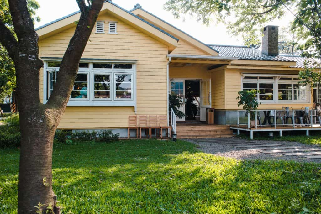 Sunny afternoon charm surrounds a cozy yellow cottage, nestled in lush greenery.
