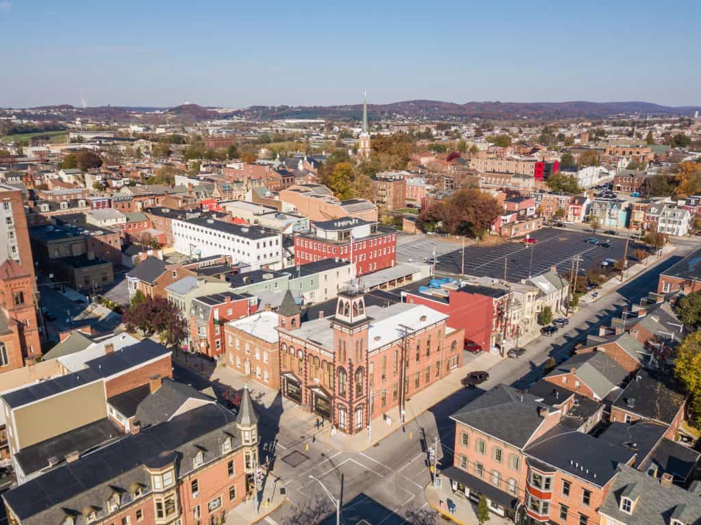 Historic charm meets urban landscape: An aerial view of a bustling American town showcases its densely packed brick buildings, church steeples, and winding streets against a backdrop of rolling hills and autumn foliage.