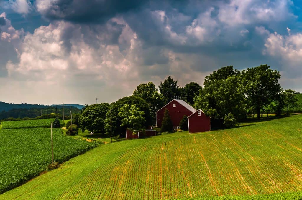 A rustic red barn nestled amidst verdant fields and rolling hills under a dramatic sky.