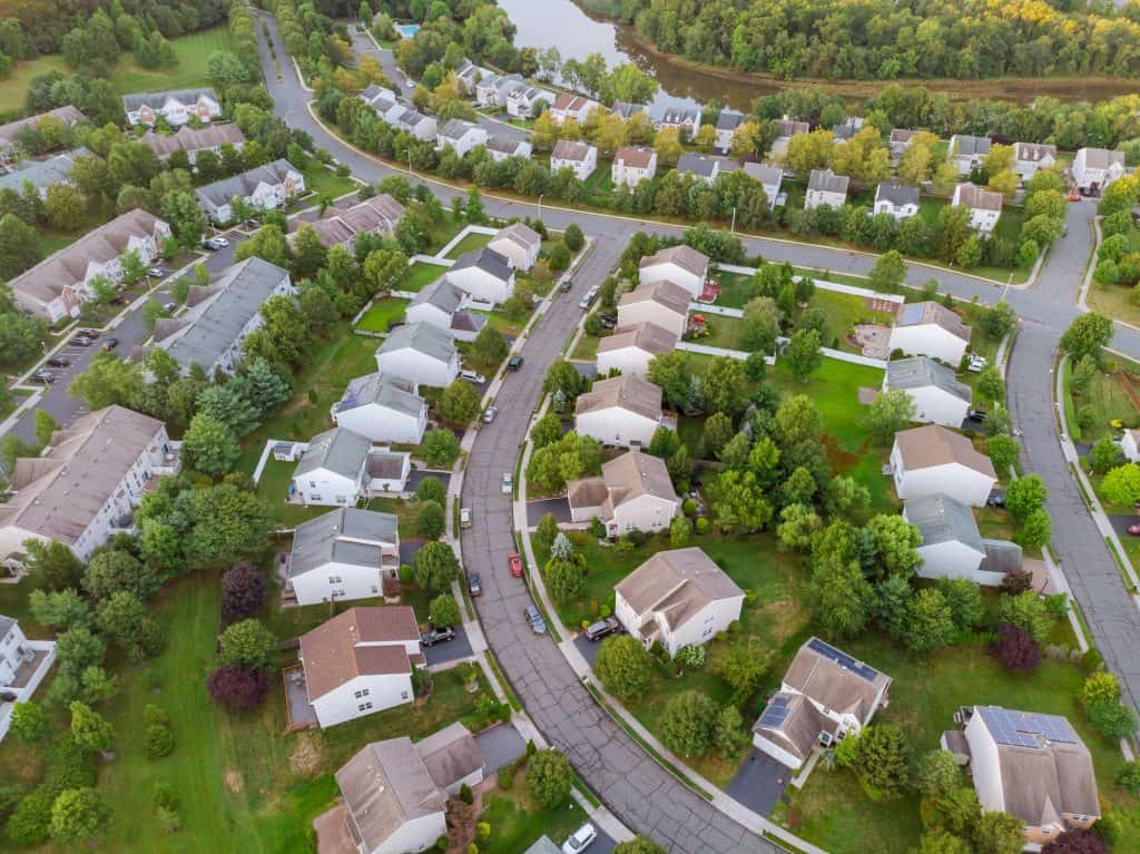 A peaceful suburban neighborhood nestled amidst lush greenery and winding roads, with a serene pond in the backdrop.