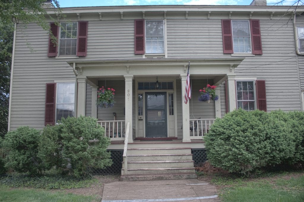 Charming historic home adorned with vibrant flowers and a proud American flag.