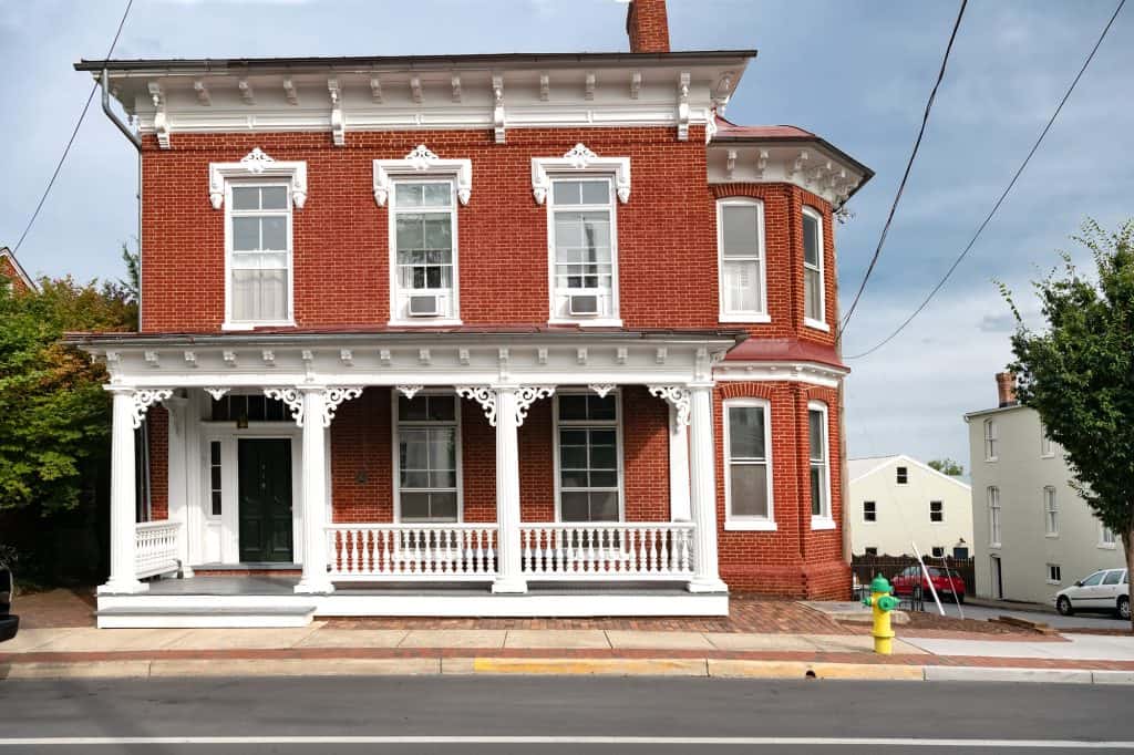 Charming Victorian red brick house with intricate white trim adorns a quiet street corner.