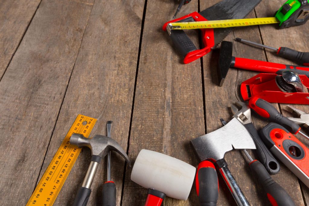 Workshop essentials: A collection of red and black hand tools including a hammer, measuring tape, rulers, and various other DIY implements arranged on rustic wooden planks.