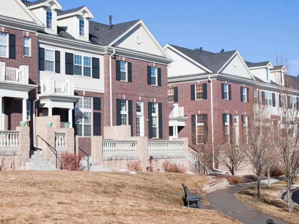 Charming brick townhomes line a peaceful suburban walkway, basking in the crisp winter sunlight.