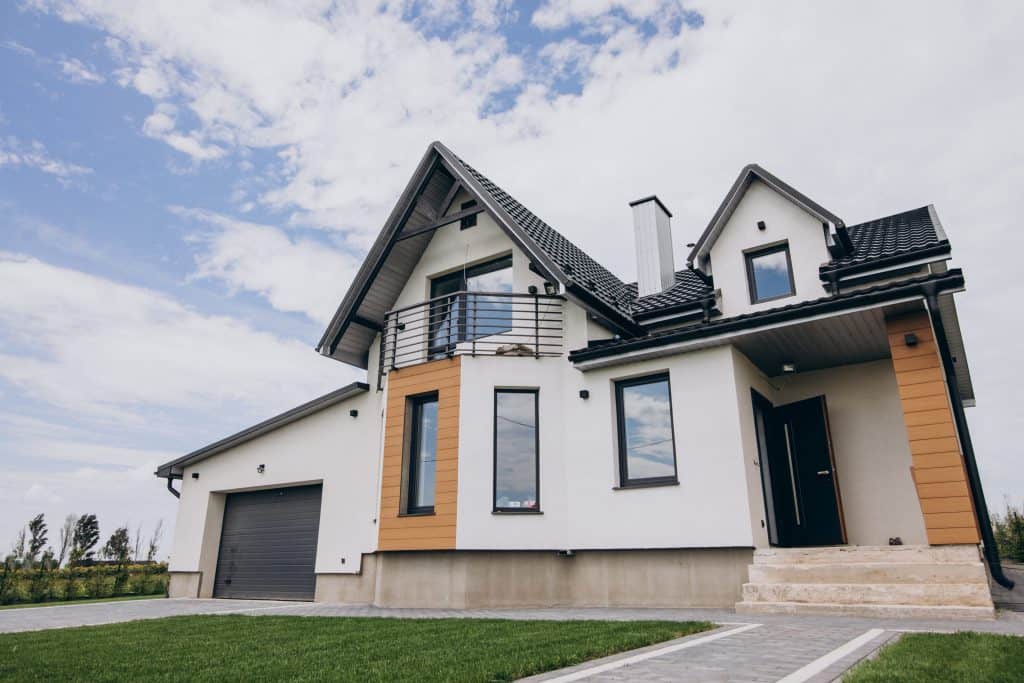 Modern two-story home featuring white and wood-tone exterior, black-trimmed windows, and a sleek balcony under bright blue skies
