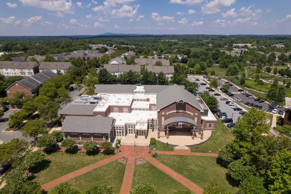 Aerial view of a suburban community center featuring brick walkways, an amphitheater, and surrounded by residential homes under a bright summer sky.