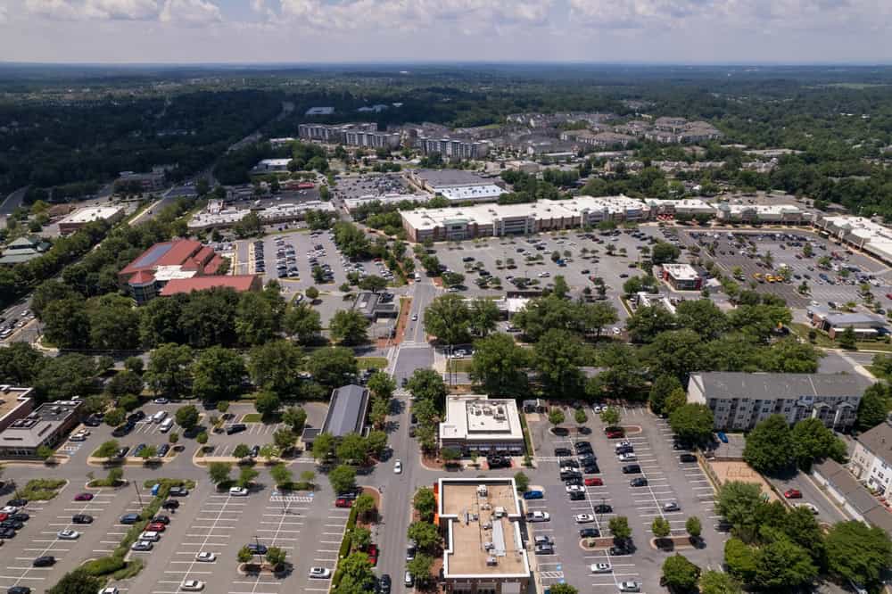A vibrant aerial view of a bustling suburban shopping and residential district, surrounded by lush greenery and filled with life.