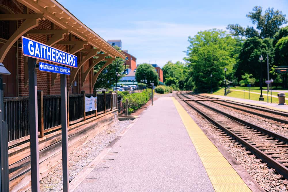 Gaithersburg train station platform on a sunny day, featuring red brick architecture, parallel train tracks, and lush green surroundings in Maryland.