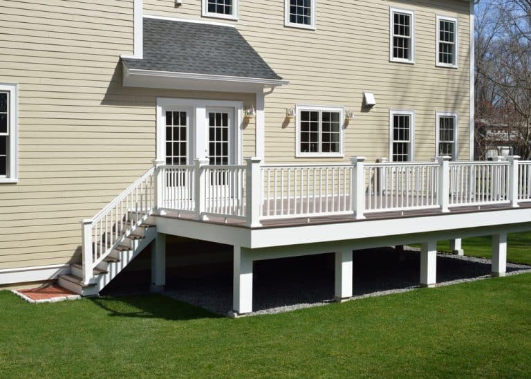 A modern deck with white railings and a staircase leading to a cozy back entrance of a beige house.