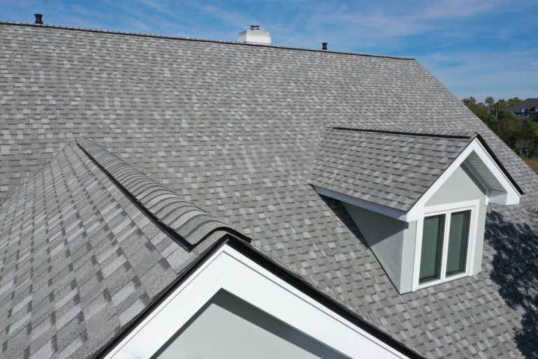 A modern roof with sleek gray shingles and a dormer window, basking under a clear blue sky.