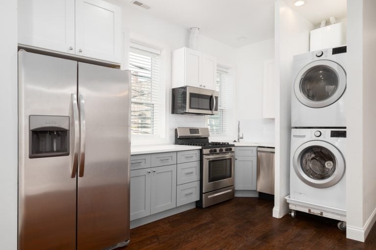 Modern kitchen with stainless steel appliances, washer and dryer, and sleek grey cabinetry.