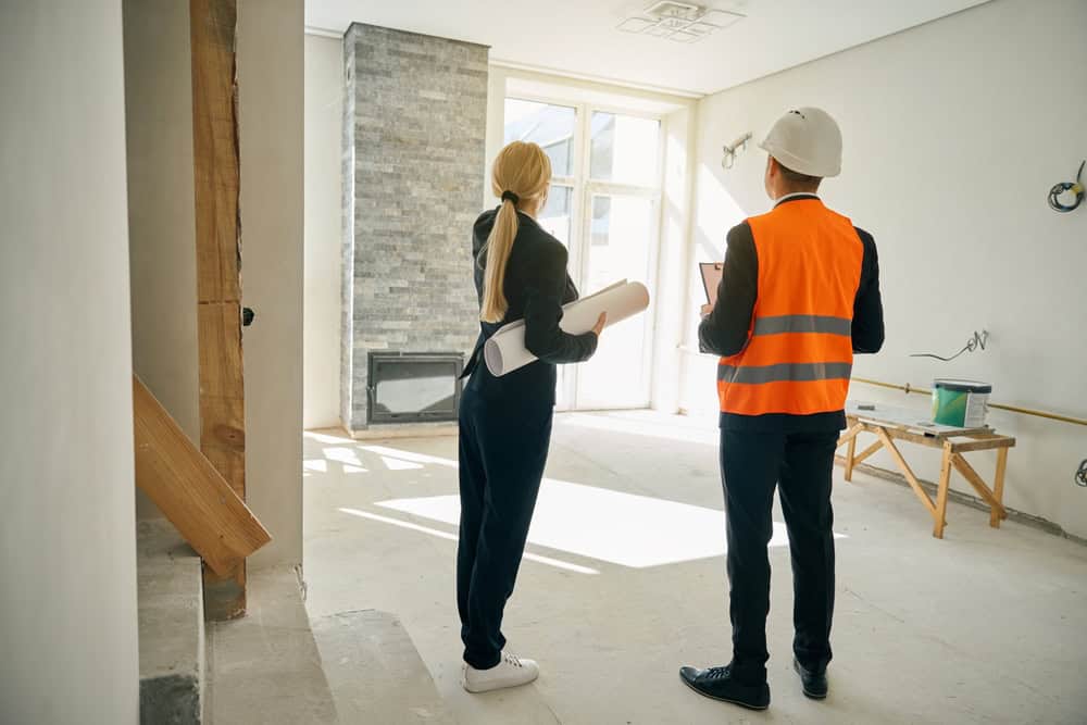 An architect and a construction worker discuss plans in a partially renovated room, bathed in natural light.