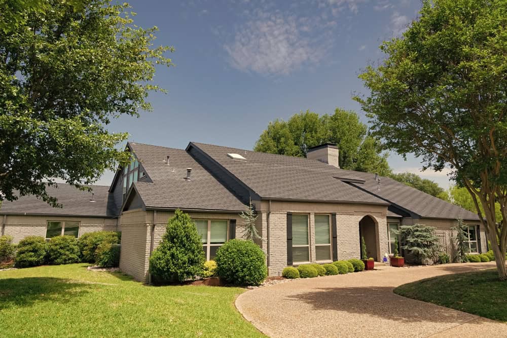A charming brick house with a well-manicured lawn and beautiful trees, perfect for a peaceful suburban retreat.
