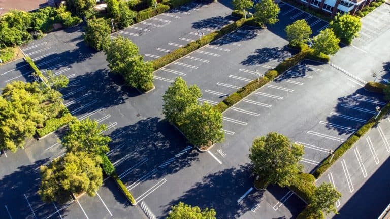 Aerial view of a nearly empty parking lot surrounded by lush green trees on a sunny day.