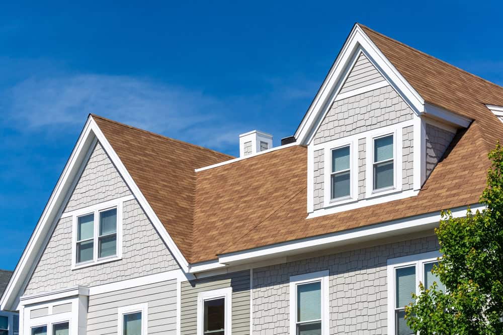 Cozy suburban home with brown shingle roof and grey siding under a clear blue sky.