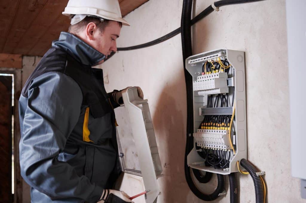 Electrician in safety gear inspecting and repairing a residential electrical panel.