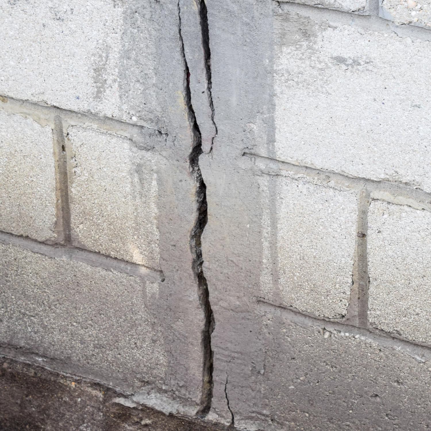A large vertical crack runs through a concrete block wall, highlighting significant structural damage.