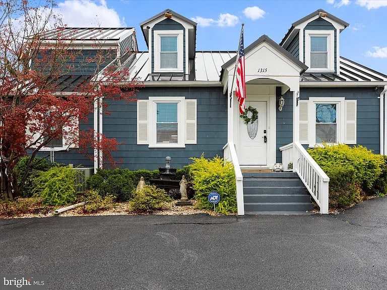 Charming blue cottage with a welcoming front porch, American flag, and vibrant landscaping.