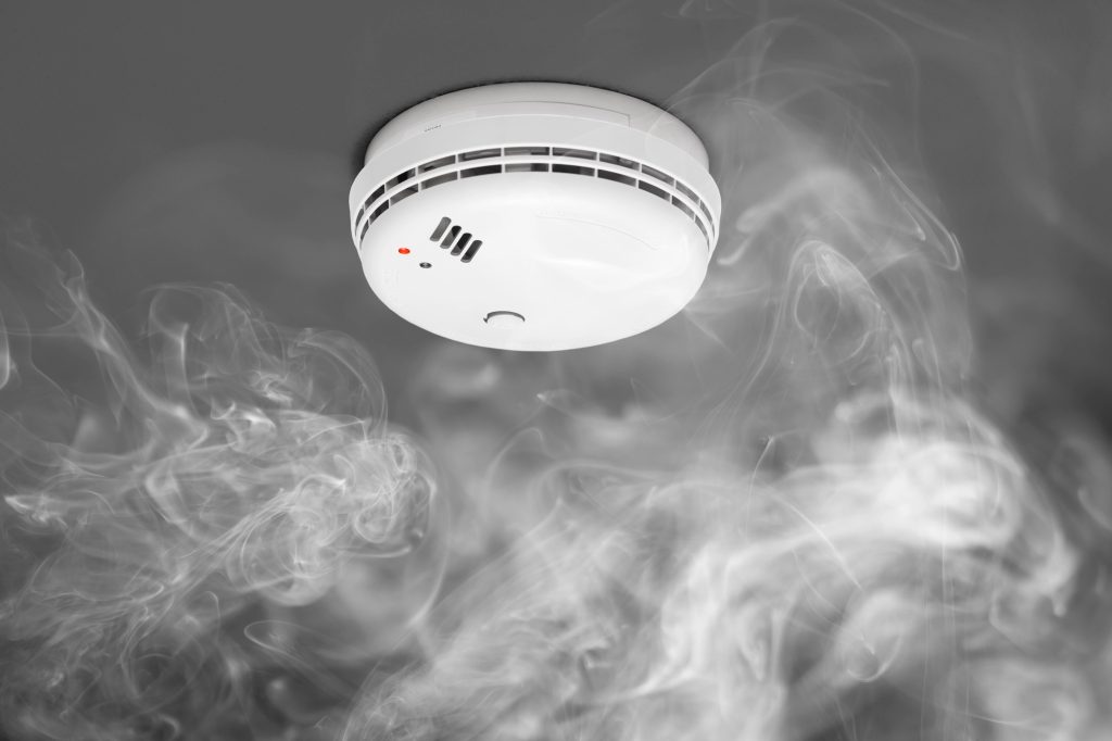 A smoke detector alerts through thick smoke, emphasizing the importance of fire safety.