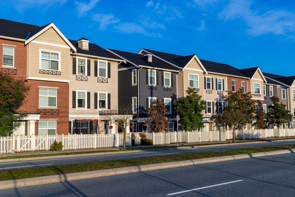Charming row of modern townhomes with white picket fences on a sunny suburban street.