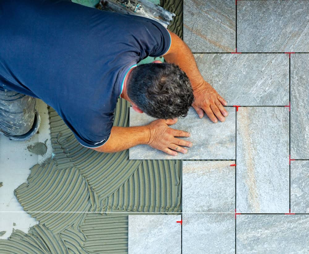 A skilled worker meticulously lays gray ceramic tiles, aligning them perfectly atop fresh adhesive for a flawless finish.